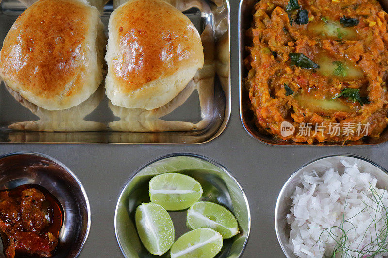 传统的印度/孟买食物Pav bhaji和新鲜出炉的面包卷一起放在不锈钢盘里。Bhaji /肉汁配上切碎的生洋葱、柠檬片和黄油